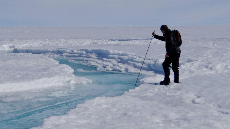 Sciences de la Terre - Un homme insère un long bâton dans un cours d'eau à la surface de la glace Sciences de la Terre